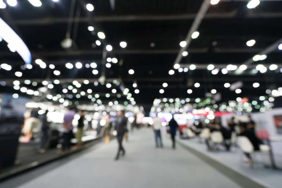 ACGrace - A blurry image of people walking around a trade show.