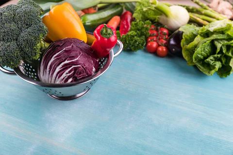 ACGrace - Fresh vegetables in a colander on a blue wooden table.