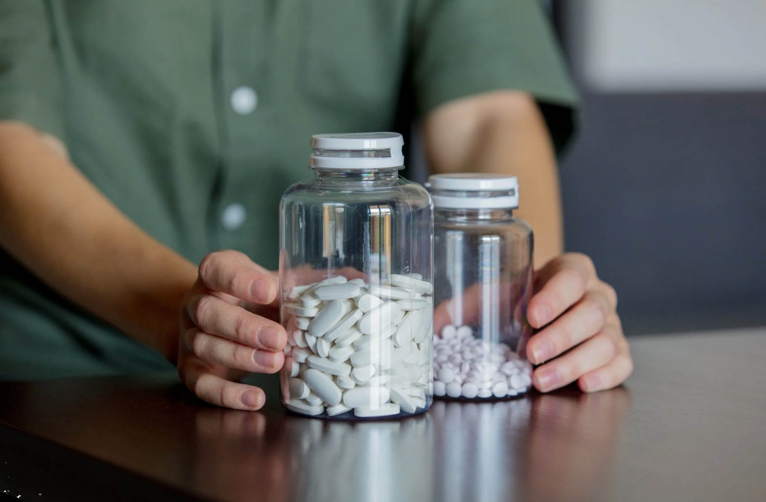 ACGrace - A person holding a bottle of pills on a table.