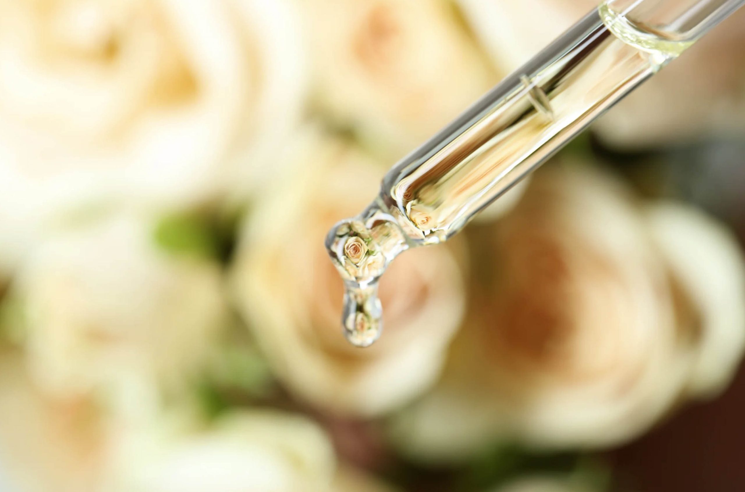 ACGrace - A syringe with a drop of oil in front of a bouquet of roses.