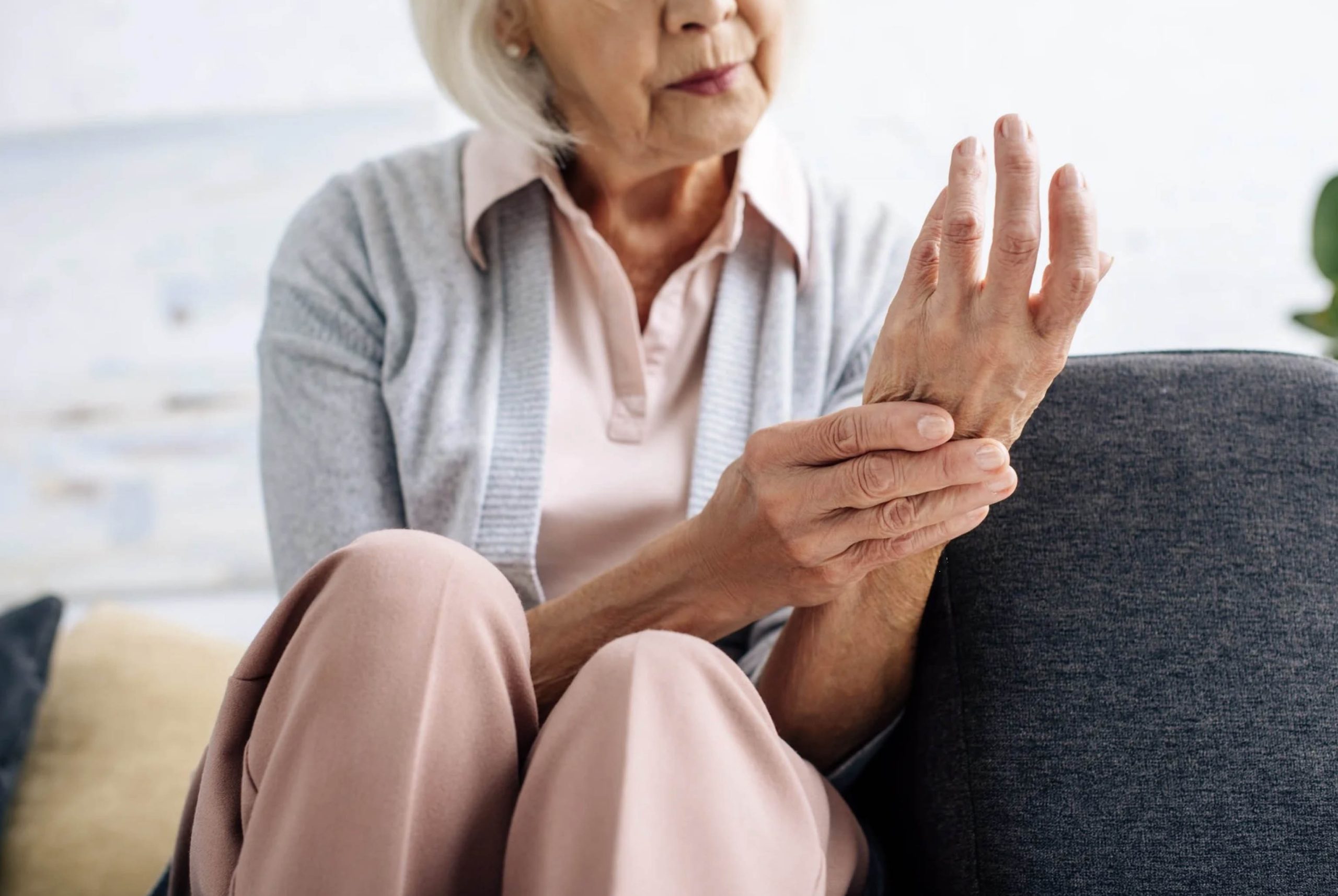 ACGrace - An elderly woman is sitting on a couch with her hand on her wrist.