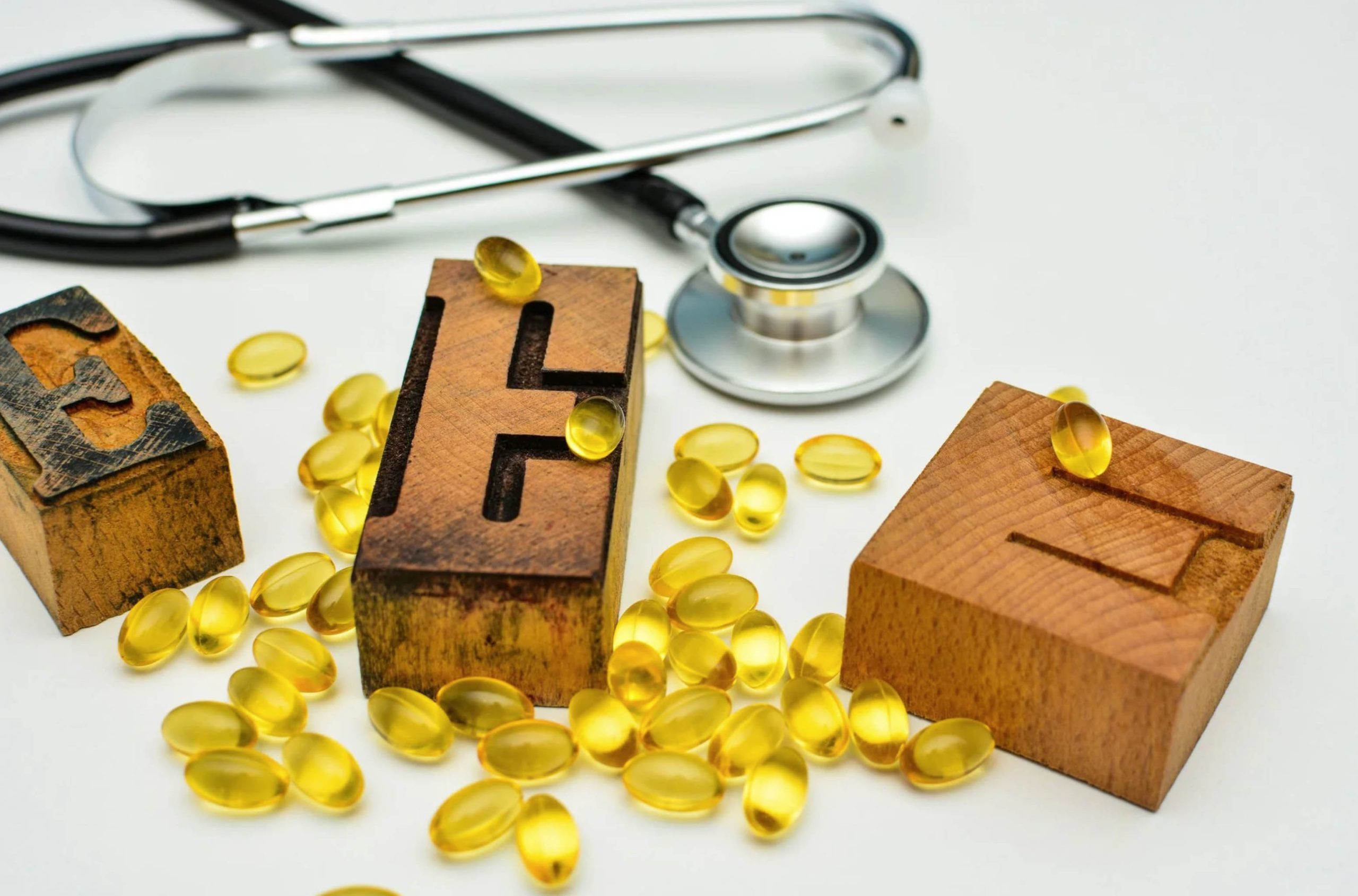 ACGrace - Vitamin e capsules and a stethoscope on a wooden block.