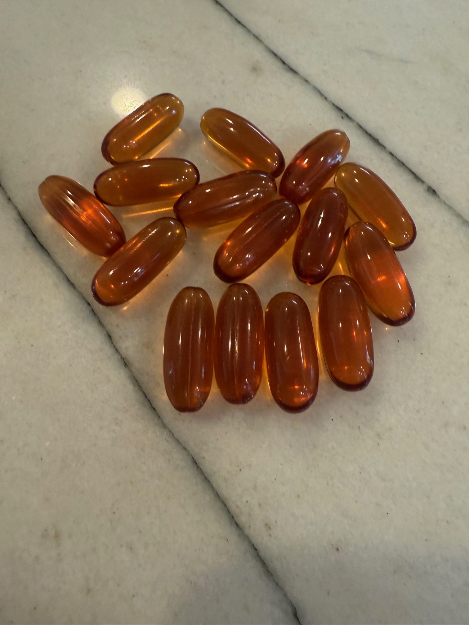 ACGrace - Fifteen translucent amber-colored softgel capsules are arranged on a light-colored, veined surface.