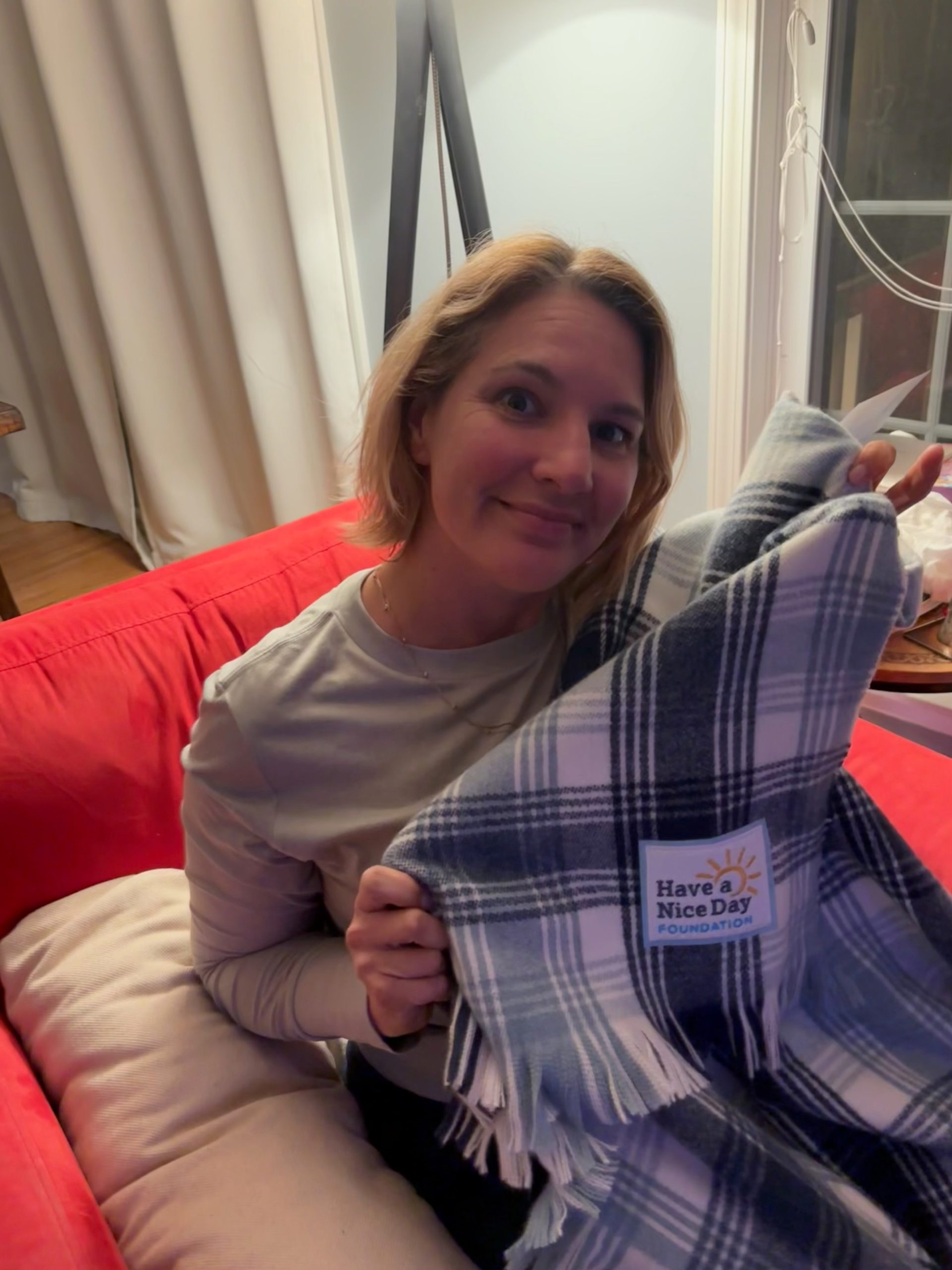 ACGrace - A person sitting on a red couch holds up a blue and white plaid blanket with a patch that says "Have a Nice Day Foundation.