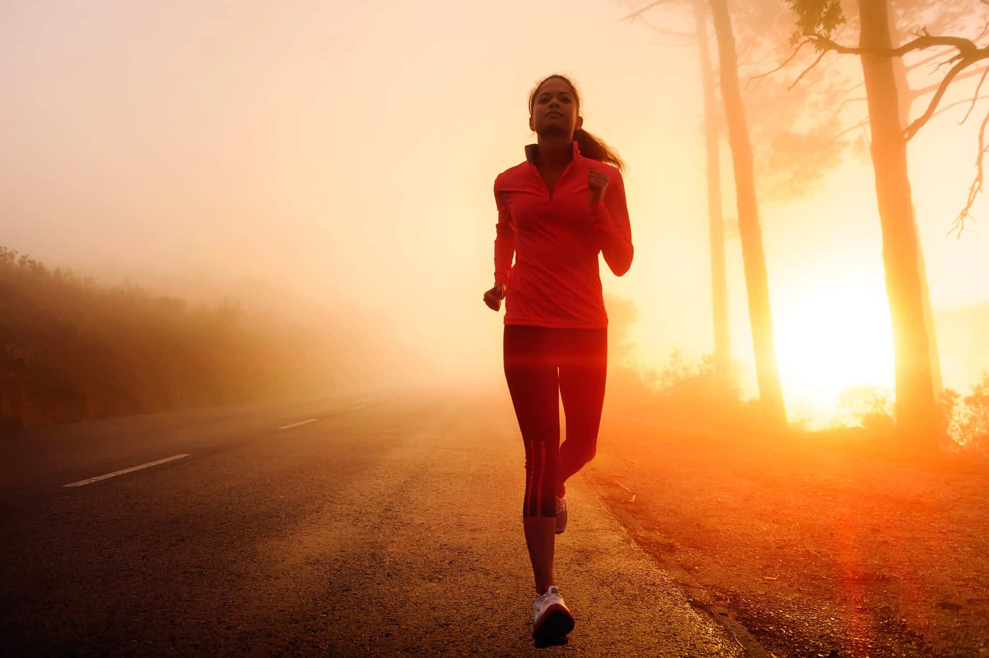ACGrace - Person jogging on a road at sunrise, with fog and sunlight filtering through trees in the background.