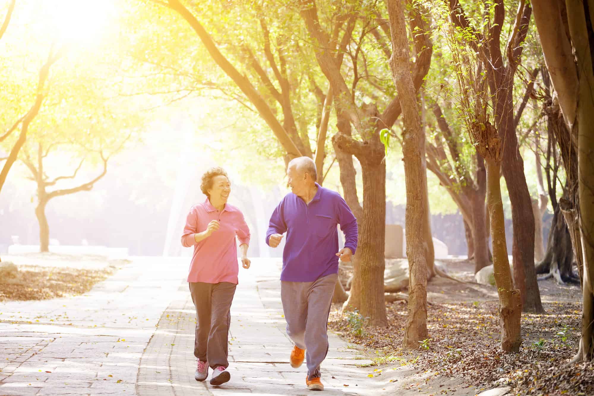 ACGrace - An older man and woman jogging together on a path through a sunlit park.