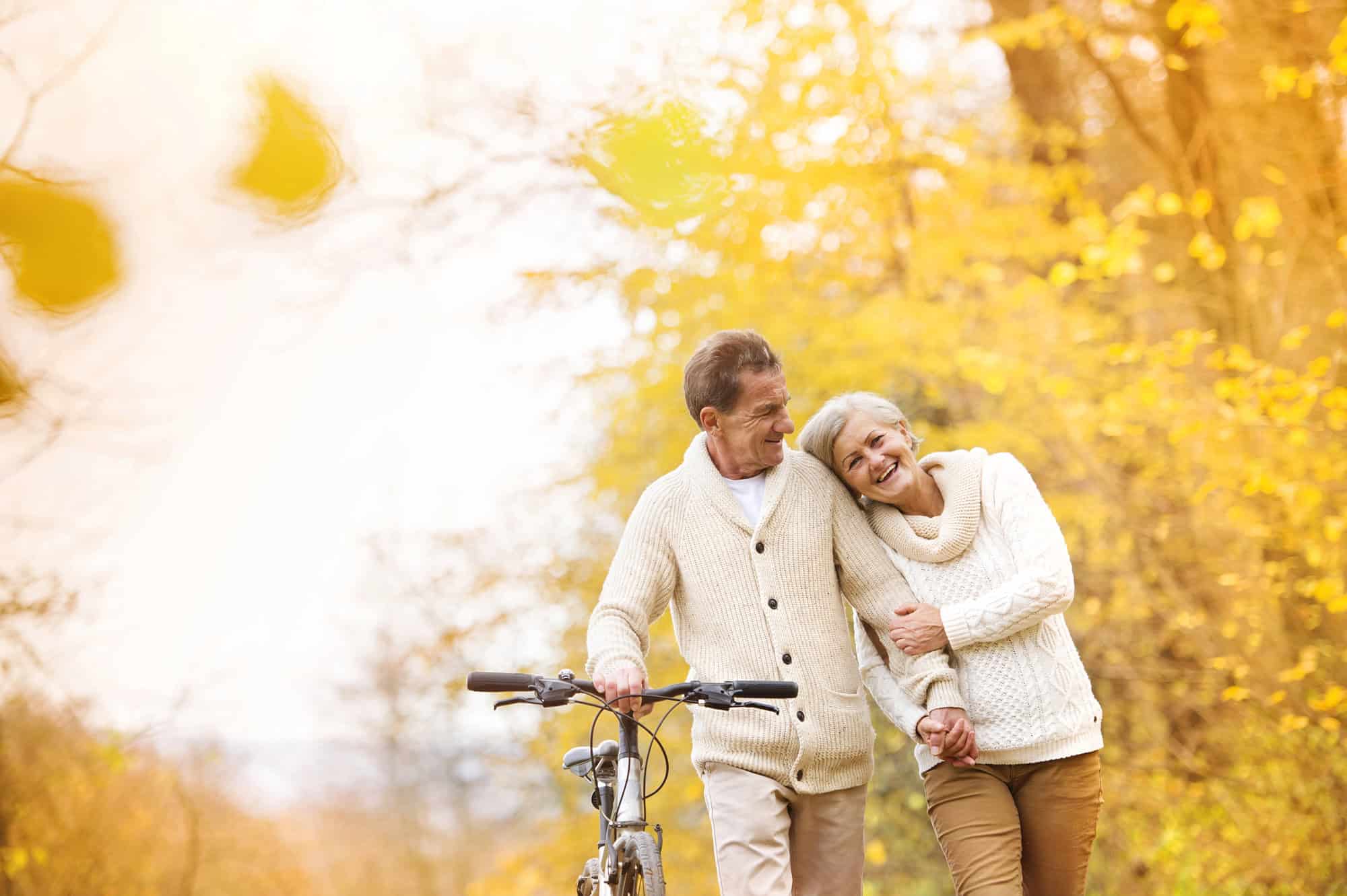 ACGrace - An older couple walking together outdoors, with the woman leaning on the man’s arm and a bicycle nearby.